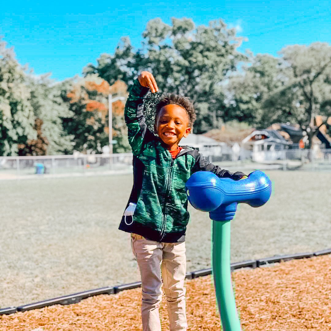An African American student plays with wood chips on a playground