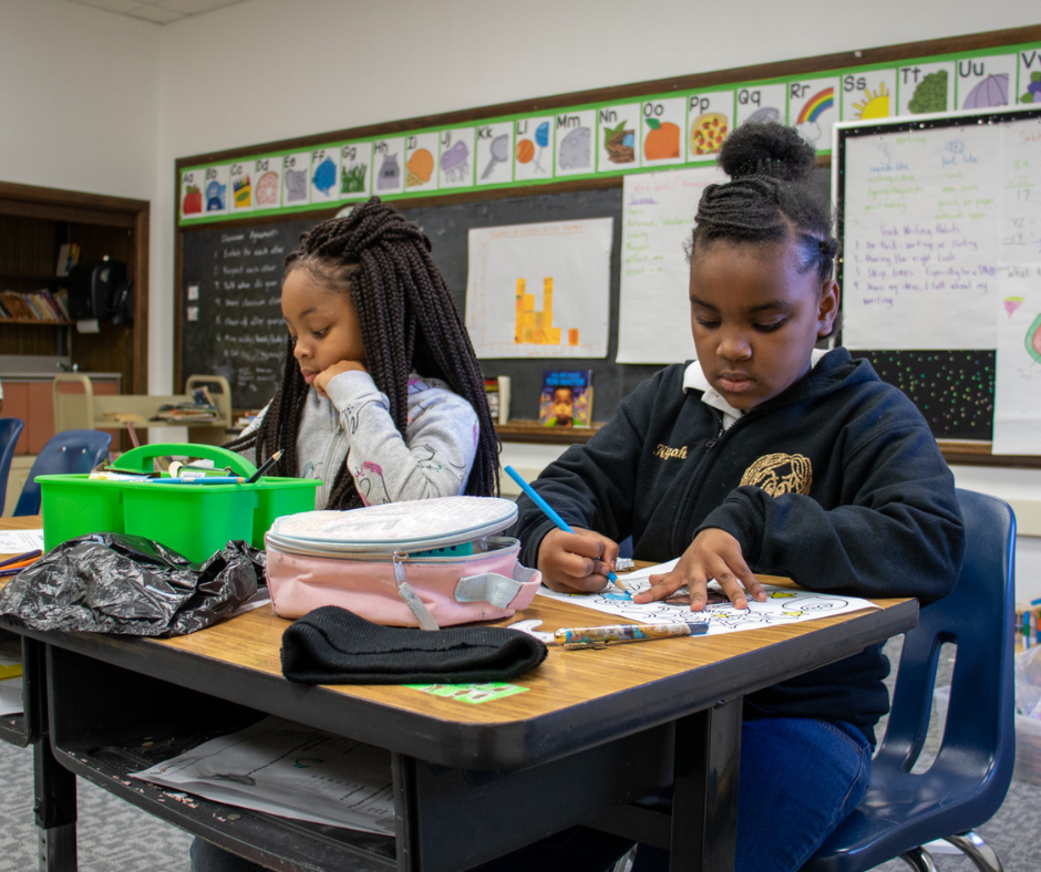 Two African-American young girls sitting at their school desks coloring