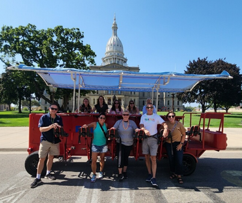 MAPSA Team posing on a pedal saloon in front of the MI State Capitol