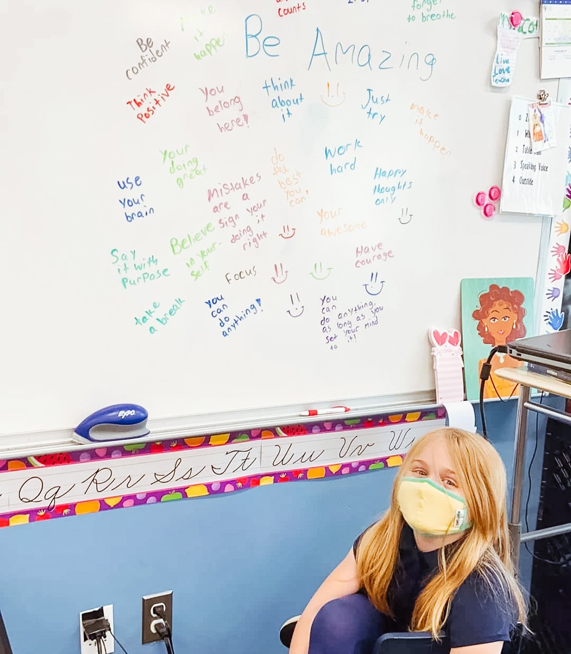 A female student sits in front of the white board where she wrote encouraging words for her classmates. 