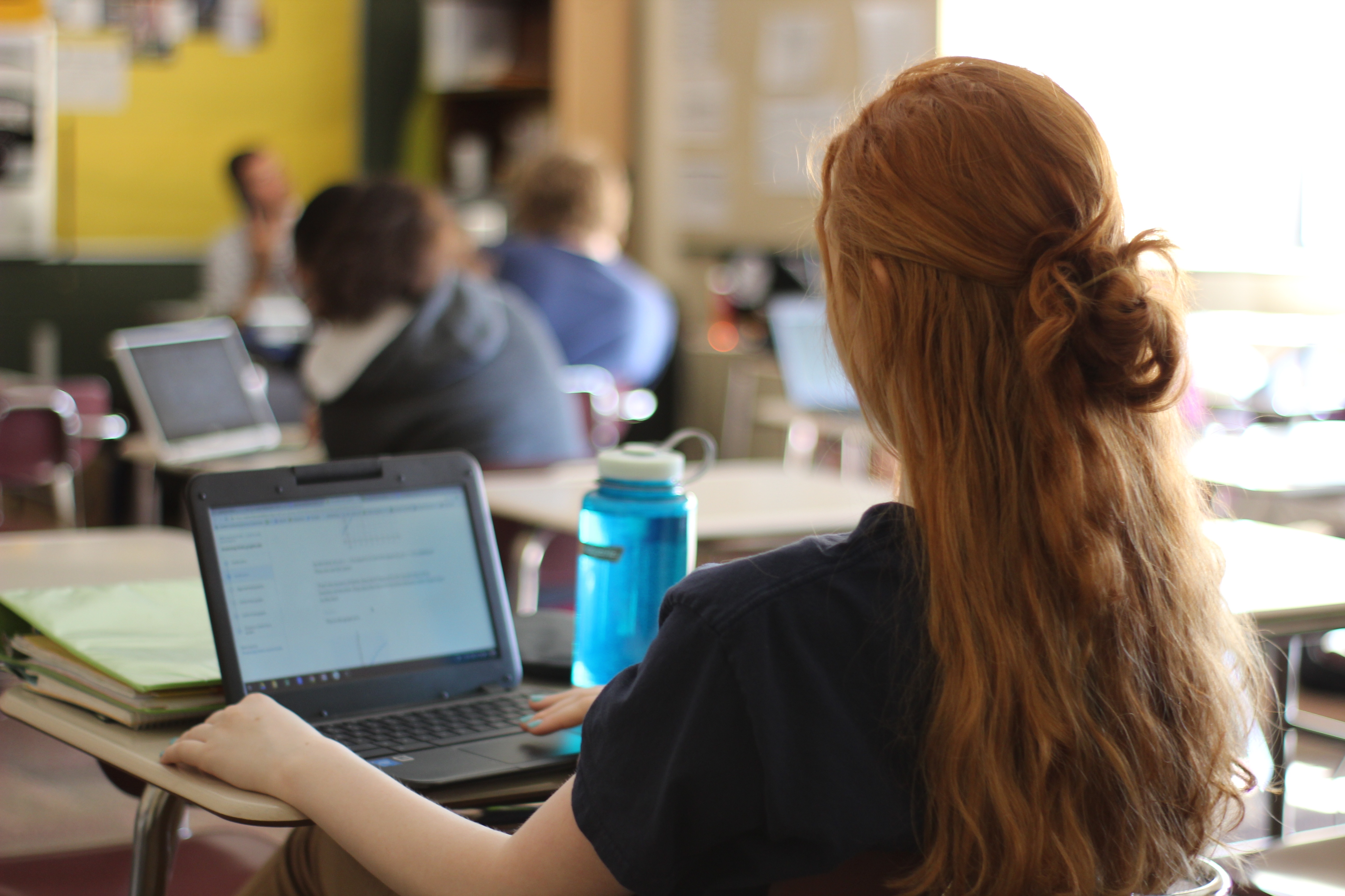 A photo of a female student typing on a computer in a K12 classroom.