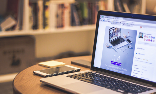 A photo of an open laptop next to a cellphone in a library.