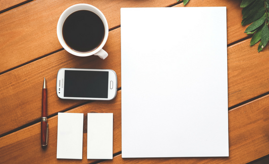 A photo of a piece of paper, cell phone, business cards, a pen and a cup of coffee.