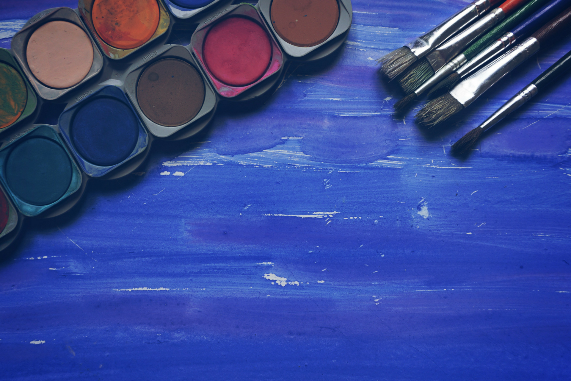 A photo of a paint set and paintbrushes atop a blue table. 