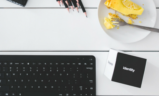 A photo of a black computer keyboard, a cube featuring the word "identity," and a plate of fresh fruit. 