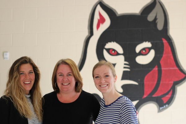 A photo of several educators posing in front of a mural of a large mascot.