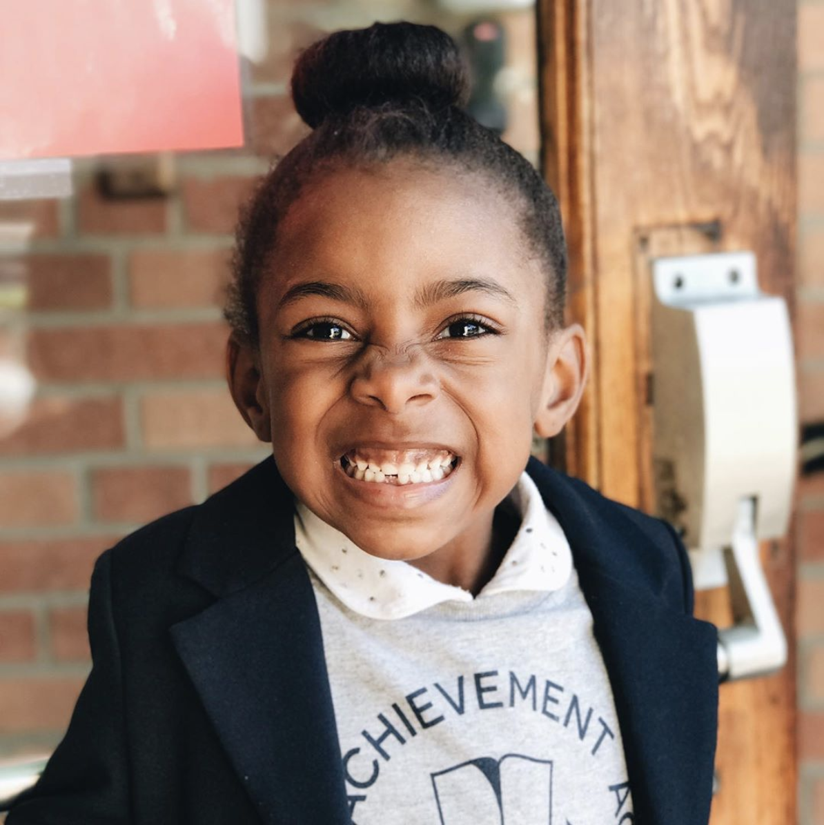 An African American student smiles at the camera while wearing a Detroit Achievement Academy shirt and blazer.