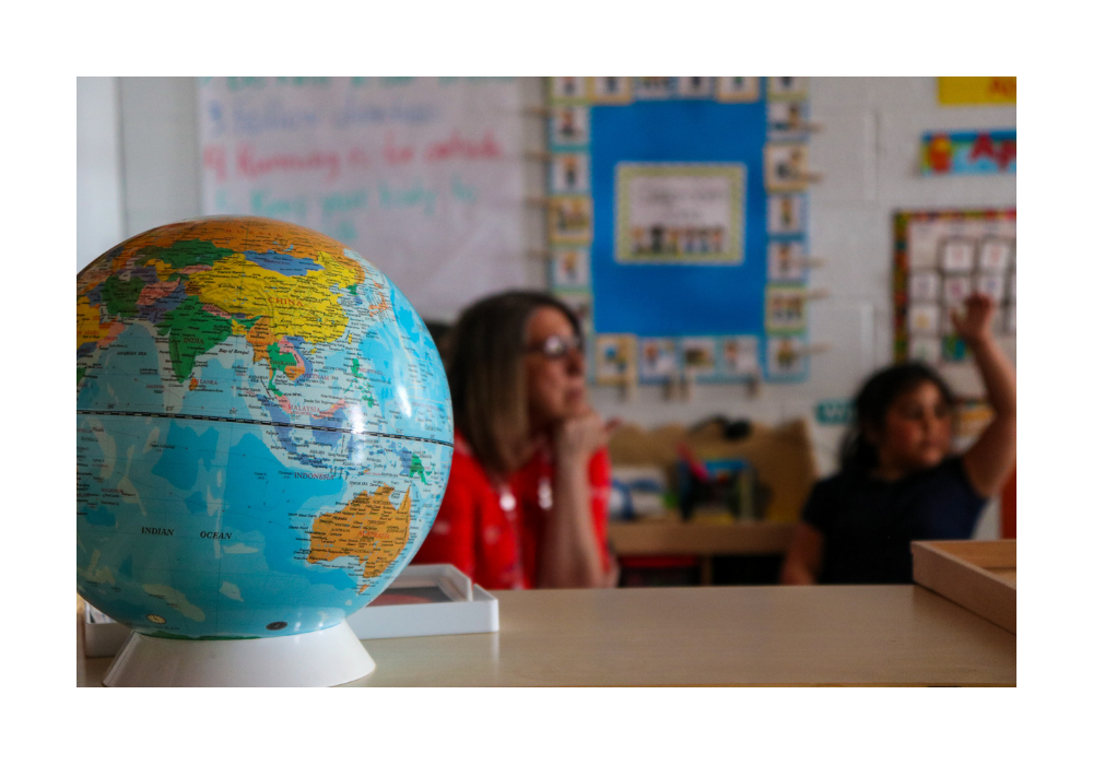 A student and teacher sit out of focus behind a globe.