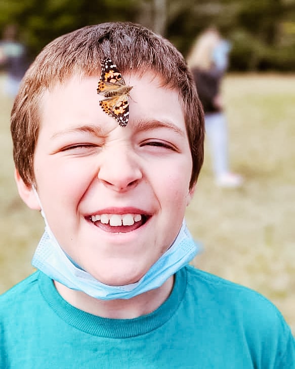 A white male student smiles while a butterfly rests on his forehead.