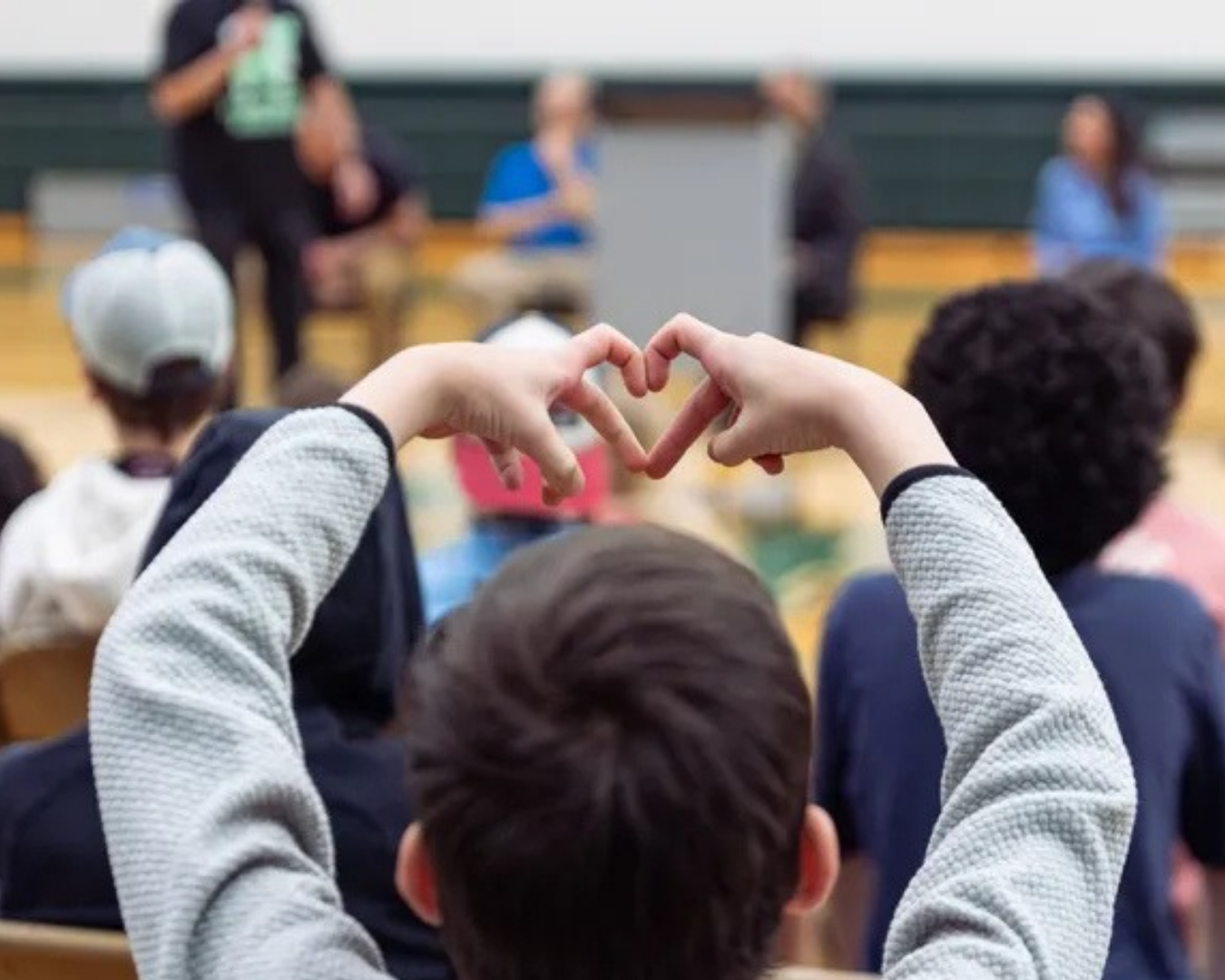 Student making a heart with hands at an assembly
