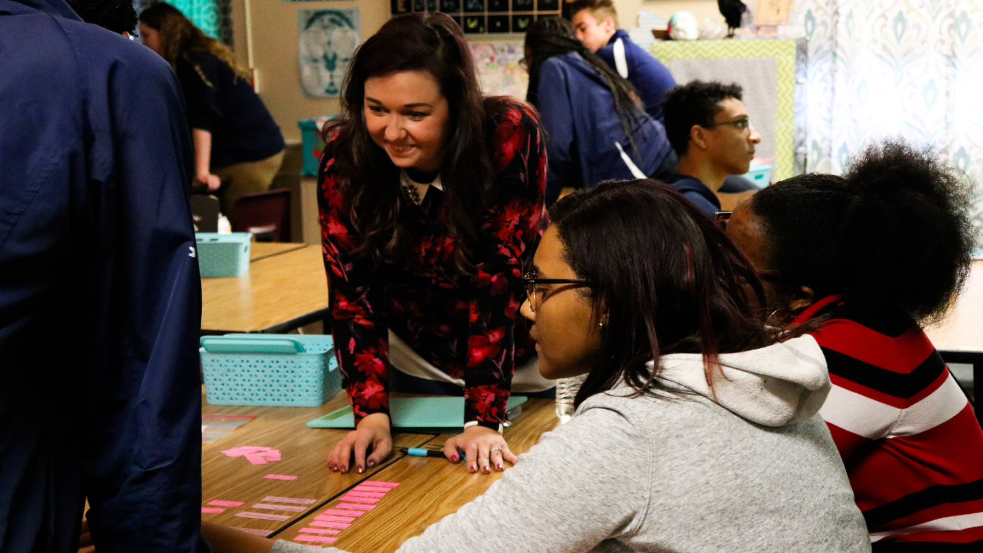 A photo of a high school classroom at Grand River Prep in Grand Rapids, where a female teacher is helping three students complete a group activity.