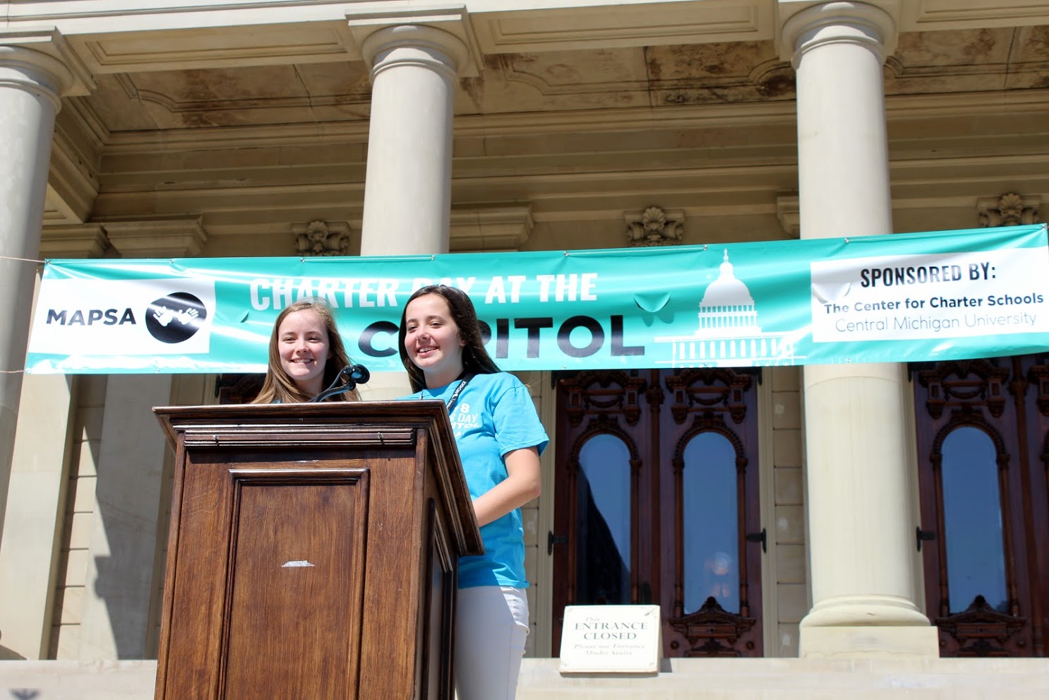 A photo of two girls giving a speech on the Lansing Capitol steps at the 2018 Charter Day at the Capitol celebration. 