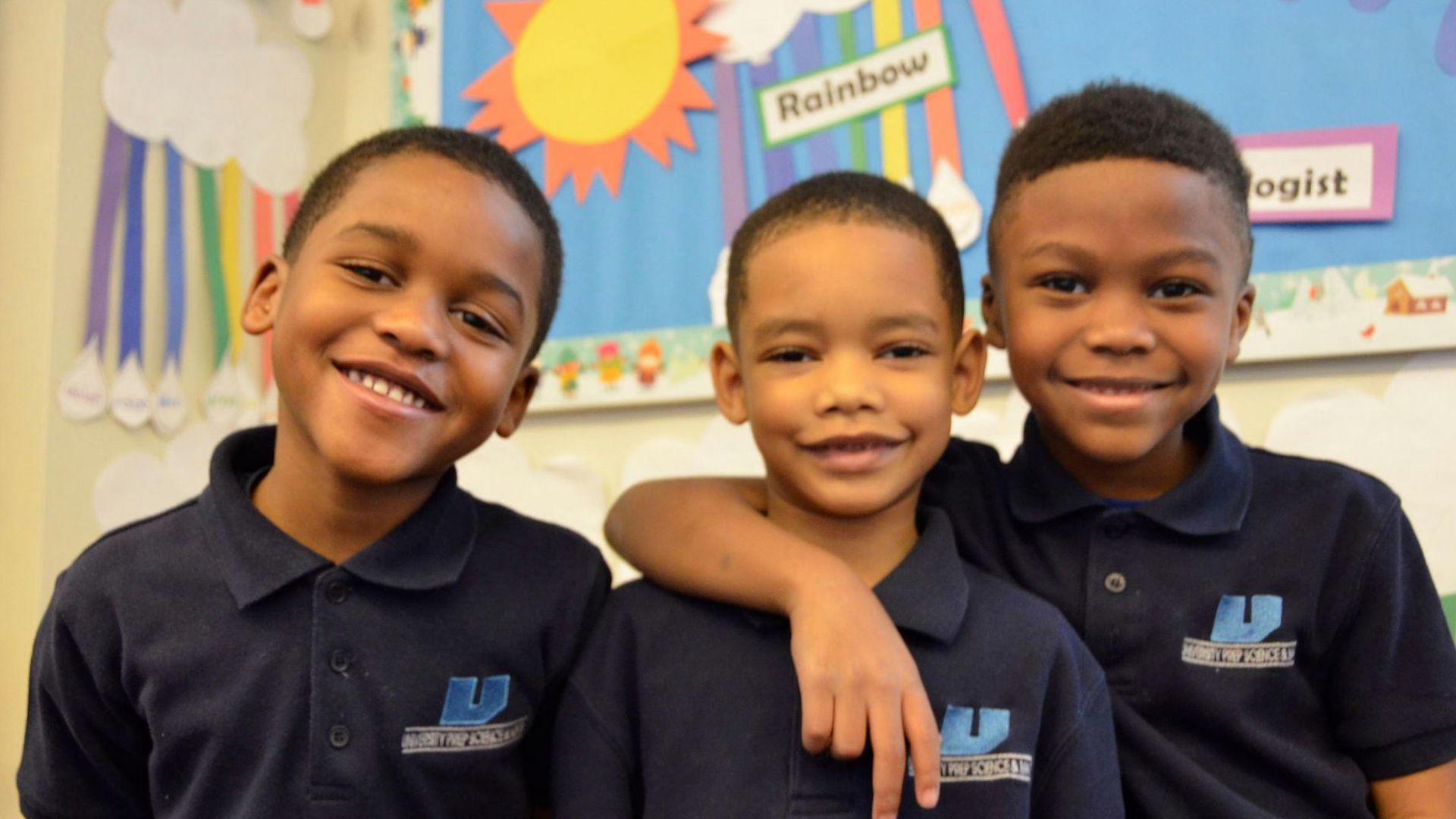 Three male African American students stand smiling at the camera. The furtherest right has his arm around the middle student's shoulders. 